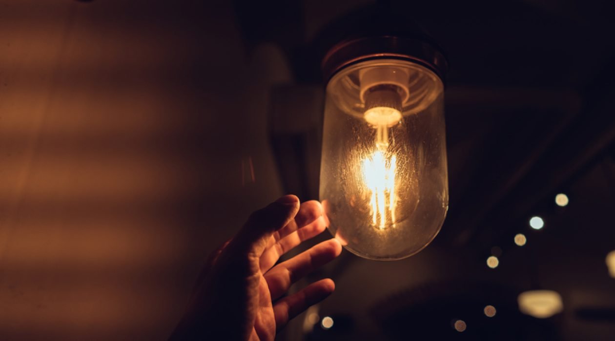 Hand reaching for a vintage light bulb. Dark and abstract concepts